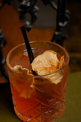 Orange alcoholic cocktail with ice on a stack of old books and dark background.