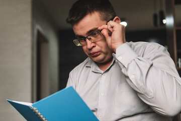 man holds a blue notebook in his hands, making notes with a pencil. The teacher, a professor with glasses, prepares the curriculum at home.