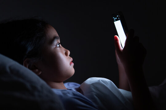 Child lying in bed using a smartphone at night. Screen time, insomnia, digital addiction concept.