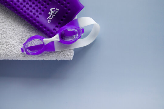 Purple swimming goggles, cap, and towel. Top view. Space for text.
