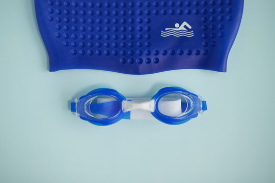 blue swimming goggles and a pool cap on a light background