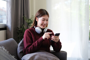A young woman sits playing on her phone in the living room of a house.