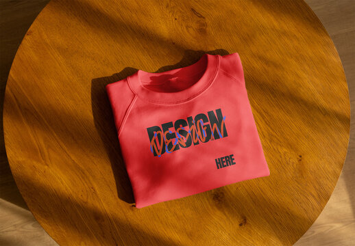 Mockup of folded sweatshirt displayed on a round wooden table 