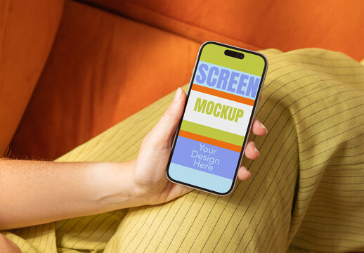 Mockup of Woman holding smartphone while sitting comfortably on a couch.