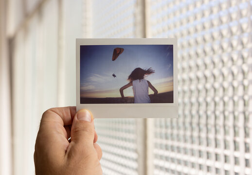 A hand holds a blank Polaroid mockup near a window with patterned light filtering through.