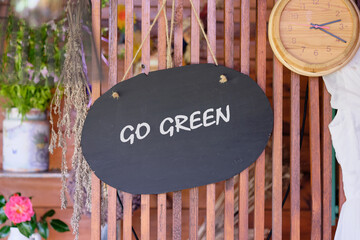 A blackboard sign with GO GREEN is hanging on a wooden lattice wall. Decorations such as plants,...