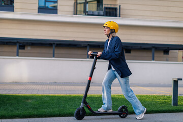 Young woman rides electric scooter on urban street wearing a yellow helmet