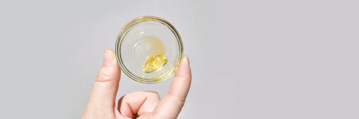 Hand holding glass with golden cannabis resin on light background.