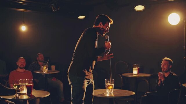 A comedian performs on stage in a dimly lit comedy club. The video captures a side angle, highlighting audience engagement and intimate atmosphere.