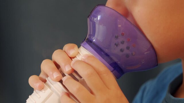 A person intently uses a purple and white respiratory therapy device, holding it to their mouth with both hands. The close-up shot emphasizes the individual's focus on improving their lung health