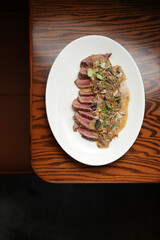 A close-up, high-angle view of a sliced steak, cooked medium-rare and showing a deep pink center, generously topped with a creamy brown mushroom sauce