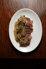 A close-up, high-angle view of a sliced steak, cooked medium-rare and showing a deep pink center, generously topped with a creamy brown mushroom sauce
