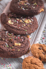 Homemade chocolate cookies with colorful sprinkles and nuts on rustic wooden background. Warm light, sweet baked dessert concept, ideal for bakery, celebration or holiday themes