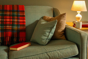 Cozy home interior with a plaid blanket and book on a couch, creating a warm, comfortable reading...