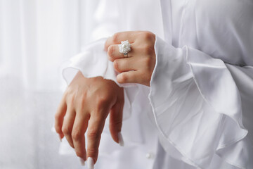 Elegant hand showcasing a stunning ring while wearing a white outfit indoors