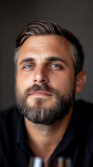 Fototapeta premium Close-up of a bearded man with green eyes and light hair against a grey background, exuding confidence and style in a portrait.
