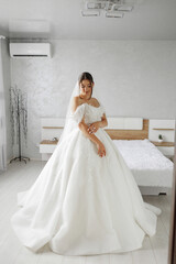 Elegant bride in white gown poses in modern room before wedding ceremony