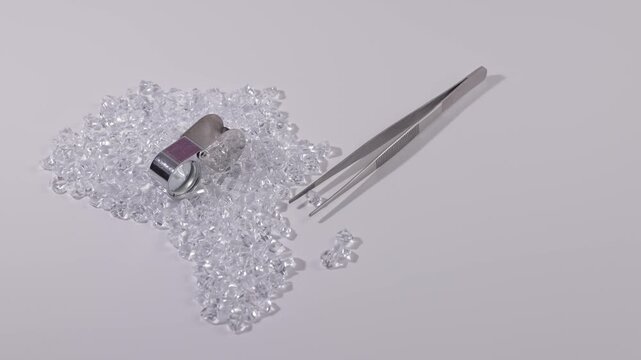 Africa continent from Sparkling cluster of raw uncut diamonds with magnifying loupe and tweezers on white background. Concept African mining industry brilliance.