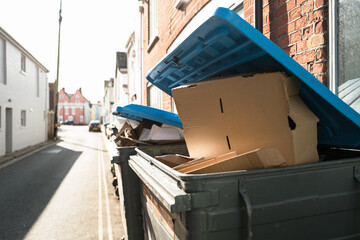 Overfilled cardboard boxes seen in a commercial waste bin, awaiting for collection down a narrow British seaside street.