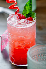 Raspberry cocktail with ice and mint close up. Close-up of pink raspberry cocktail with ice, mint leaves, and red straw served with umbrella decoration.