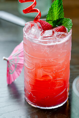 Raspberry mojito with mint and ice close up. Refreshing raspberry mojito with mint leaves, ice cubes, and red straw served on wooden table.