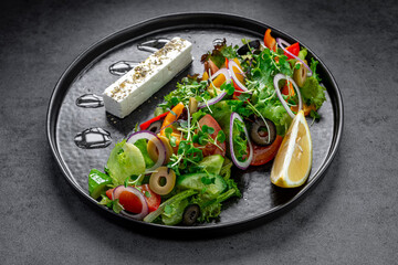 Greek salad with feta cheese and fresh vegetables. Black and green olives, cucumbers, tomatoes, and red onion rings served with lemon.