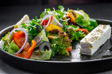Greek salad with feta cheese and olives side view. Side view of Greek salad with feta cheese, vegetables, and olives served with lemon on a black plate.