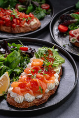 Bruschetta with salmon, caviar, and avocado slices. Bruschetta with salmon, avocado, and red caviar served with salad and lemon wedge on black plate.