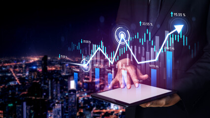 A businessman uses a digital tablet to analyze financial data represented by graphs and metrics,...