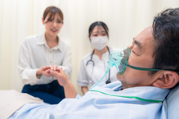 人工呼吸器をつけた家族のお見舞いをする若い女性