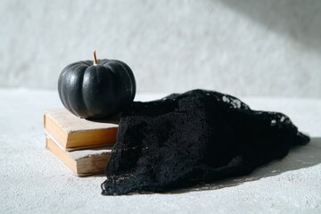 Black Pumpkin and Lace Cloth on Wooden Books in Soft Light