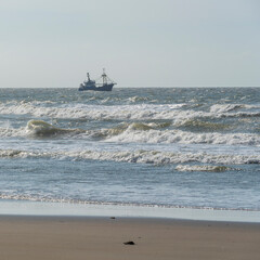 single ship is sailing on the North Sea, ship, sails and waves shine in the evening light, North Sea beach before sunset with waves of the ocean