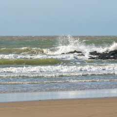 Storm build big waves, they break on the stone wall at the beach, stormy waves shine in the evening light, North Sea beach before sunset with waves of the ocean