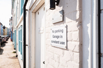 Shallow focus of a No Parking sign seen attached to a pastel coloured terraced house down a narrow...