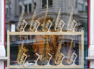 Display of various saxophones arranged in a wooden showcase, reflecting light from the street, showcasing musical instruments in a vibrant urban environment with artistic flair