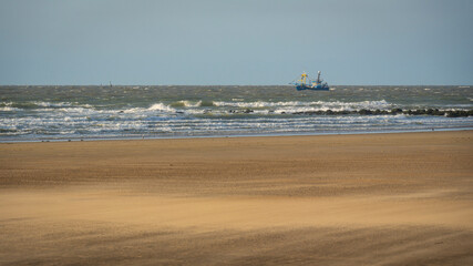 single ship is sailing on the North Sea, ship, sails and waves shine in the evening light, North Sea beach before sunset with waves of the ocean