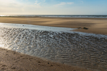 evening light and water makes structures in the sand at the North Sea, natural art on the sandy beach, a stream on the beach forms water and sand, wave-shaped depressions form a beautiful pattern