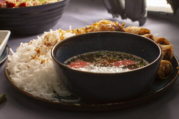 On the table, there is a plate filled with rice next to a bowl of warm soup accompanied by various side dishes