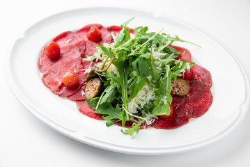 Beef carpaccio with arugula, cherry tomatoes, Parmesan cheese, and olive oil on a white plate. Classic Italian appetizer, fresh and elegant presentation.