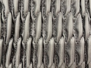 Close-up of gray quilted fabric texture with a geometric pattern. Detailed textile surface showing soft padded stitches and shiny synthetic material, background for fashion or upholstery design.