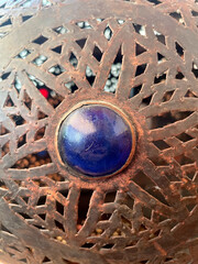 Close-up of an ornate metal lantern with a blue glass gem centerpiece.Antique bronze latticework design with rustic texture and decorative detail, traditional handmade Middle Eastern or Moroccan craft
