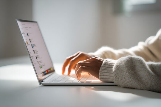 Person sitting at a white desk, only hands visible typing on a laptop keyboard