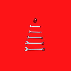 Christmas tree made of wrenches decorated with balls on a red background. New Year banner with tools. Postcard with place for greeting text for happy new year with industrial holiday concept. Close-up