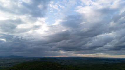 Dramatic cloudy sky over a vast green landscape seen from above. A moody and atmospheric view capturing the beauty of nature, weather, and the endless horizon