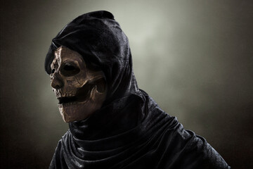 Creepy figure in hooded cloak over dark misty background at night