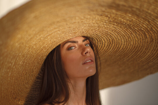Close-up portrait of woman in giant straw hat looking up in soft warm light. Elegant summer aesthetic