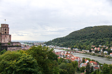 panoramic shot showing the tower of the medieval heidelberg castle to the left and the river, bridge and city with its green mountains to thee right on a hazy fallday