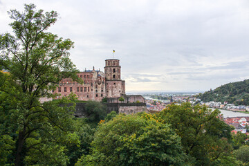 wide shot showing the medieval heidelberg castle to the left and the river, bridge and city with its green mountains to thee right on a misty fallday