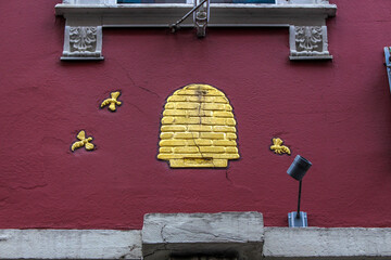 golden relief shows a beehive and three bees on a red house facade, which gives a noble expression