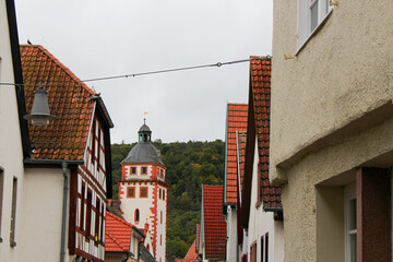 red-white stone church tower in an old german town surrounded by old medieval half-timbered (fachwerkhäuser) buildings and a green mountain in the background